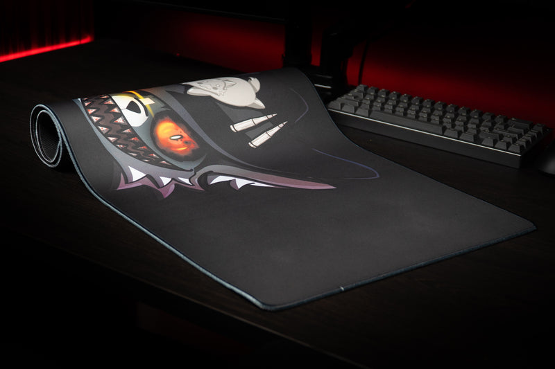 Iddqd Chonk Mat gaming deskmat partially rolled on a dark desk, showing the cowboy cat artwork and stitched border.