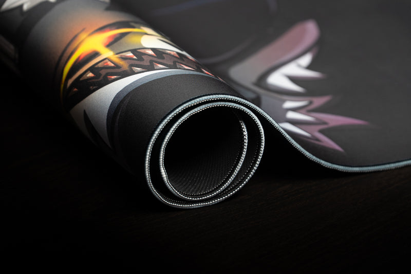 Close-up of Iddqd's Chonk Mat deskmat rolled to show the stitched edge, black backing, and printed cat artwork.