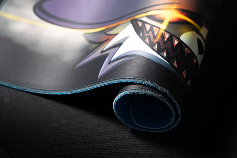 Close-up of Iddqd's Chonk Mat playmat rolled to show the blue stitched edge, black backing, and sharp-toothed cat artwork.