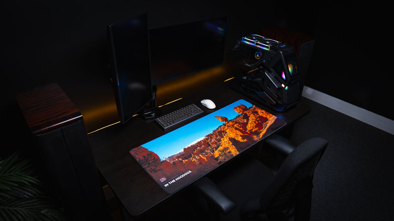 Angled view of the In the Hoodoos Bryce Canyon National Park deskmat displayed on a premium gaming desk, showcasing vibrant hoodoo rock formations, America 250 branding, and a clean PC setup.