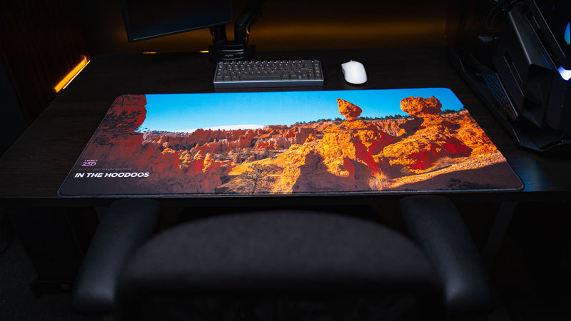Full desk setup featuring the In the Hoodoos Bryce Canyon National Park deskmat with vibrant hoodoo rock formations, America 250 branding, and premium stitched edges.