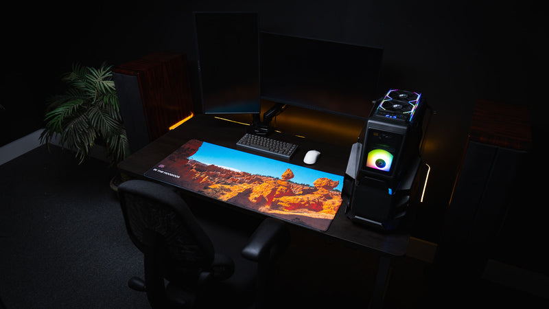 Gaming desk setup featuring the In the Hoodoos Bryce Canyon National Park deskmat with vibrant hoodoo formations, premium stitched edges, and a clean dual-monitor workspace.