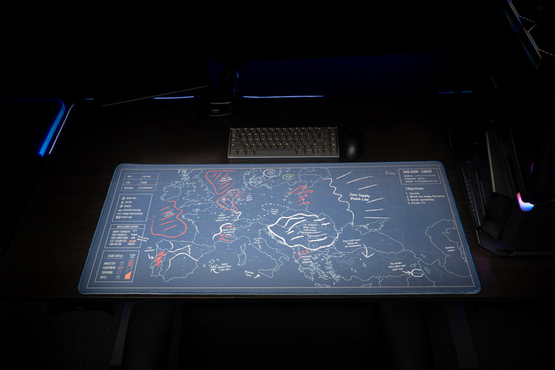 Front view of the Jaush Vague Concepts of a Plan deskmat displayed beneath a keyboard and monitors in a blue-lit setup.