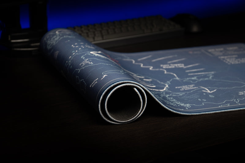 Rolled Jaush Vague Concepts of a Plan deskmat showing its stitched edge, blue map surface, and black underside.