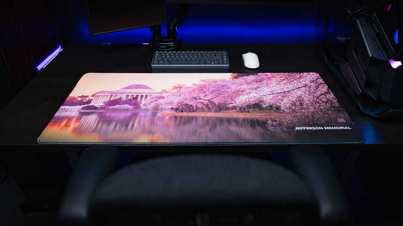 Jefferson Memorial America 250 deskmat displayed on a desk setup with cherry blossoms, reflecting water, and monument artwork.