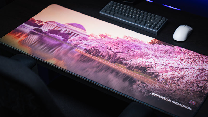 Angled view of the America 250 Jefferson Memorial deskmat featuring the Jefferson Memorial framed by vibrant cherry blossoms and their reflections across the Tidal Basin on a premium gaming desk.