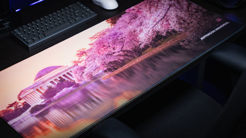 Perspective view of the America 250 Jefferson Memorial deskmat showcasing the Jefferson Memorial, blooming cherry blossoms, and reflections across the Tidal Basin on a premium gaming desk setup.
