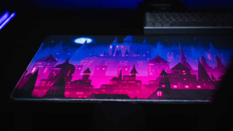 Angled view of Chroma Kingdom deskmat glowing beneath blue and magenta lighting