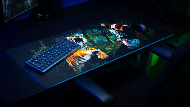 Official Rust Jungle Ambush deskmat displayed with a mechanical keyboard and gaming mouse, featuring a tiger attacking a survivor in a jungle.