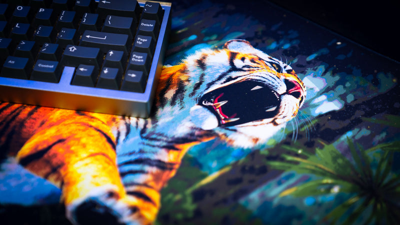 Close-up detail of a roaring tiger on the official Rust Jungle Ambush deskmat with a mechanical keyboard positioned above the artwork.