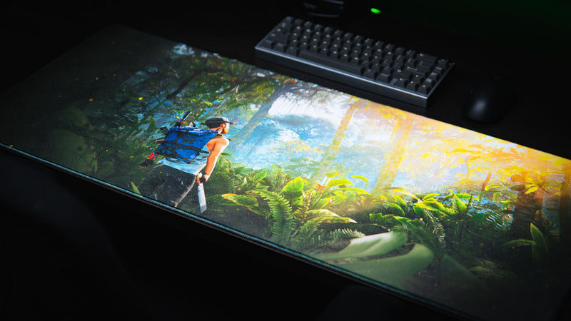 Jungle Exploration premium gaming deskmat displayed on a desktop setup, featuring a lone explorer trekking through a lush sunlit jungle.