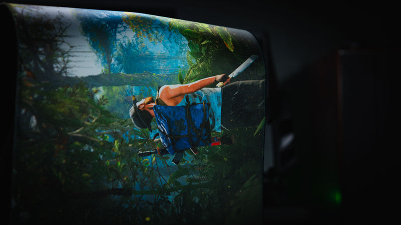 Close-up of the Jungle Exploration deskmat draped over a chair, highlighting the Rust survivor artwork, flexible cloth construction, and stitched edge.