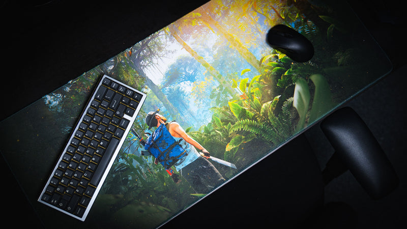 Angled desktop view of the Jungle Exploration deskmat featuring a Rust survivor trekking through a vibrant tropical jungle with keyboard and mouse.