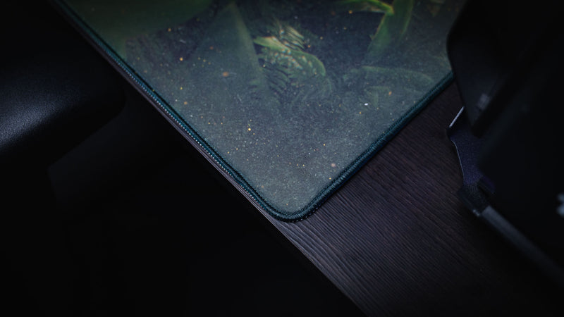 Close-up of the Jungle Exploration gaming deskmat featuring premium stitched edges, rounded corner stitching, and subtle rainforest artwork.