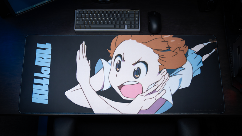 Gaming desk setup featuring the Kill la Kill “Mako’s Fury” anime deskmat with energetic character artwork and minimalist black design.