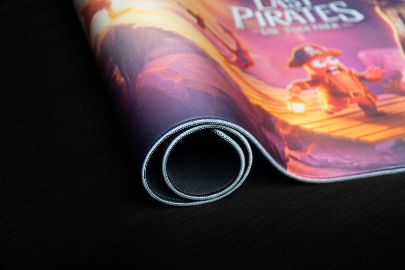 Rolled Bridge Escape desk mat showing its stitched edge, rubber underside, and colorful pirate artwork