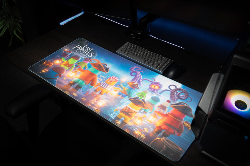 Kraken Tide desk mat beside a keyboard and RGB-lit PC, showing the pirates and sea creature