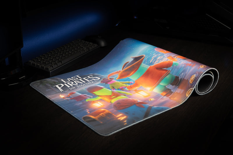 Partly rolled Kraken Tide desk mat on a dark gaming desk showing pirate crew artwork