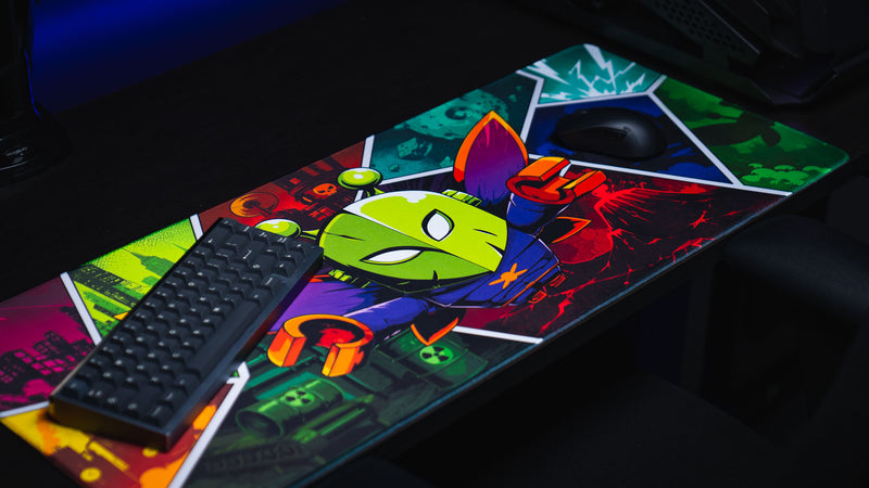 Angled gaming setup featuring the Lure of the Night deskmat with a colorful cartoon moth character and comic-inspired Rust biome artwork.