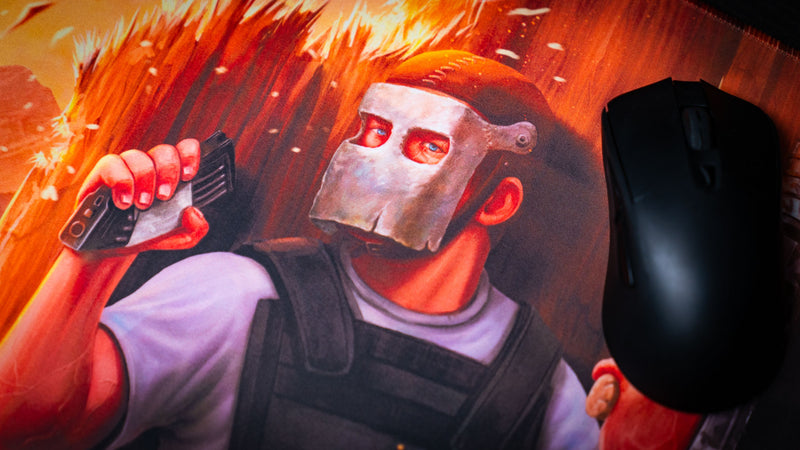 Close-up of the main scene Rust deskmat featuring the masked defender holding a radio beside a gaming mouse, showcasing the vivid artwork, premium print quality, and smooth stitched-edge gaming mouse pad surface.