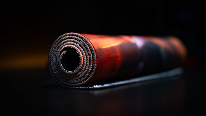 Rolled Take Main Scene deskmat highlighting its flexible premium construction, stitched edges, durable rubber base, and vibrant high-definition artwork, ready for storage or travel.