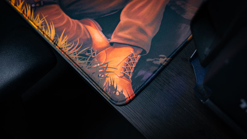 Close-up of the Main Scene Rust deskmat featuring premium stitched edges, detailed artwork around the survivor's boots, and a smooth gaming surface with a durable non-slip rubber base.