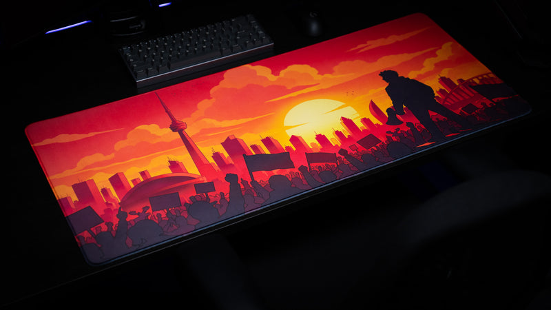 Angled view of the MapleTakes Golden Hour Defiance gaming deskmat with vivid Toronto sunset and protest artwork