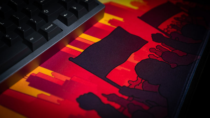 Close-up of protest sign artwork on the MapleTakes Golden Hour Defiance gaming deskmat beside a mechanical keyboard