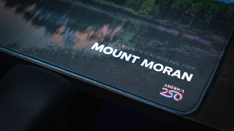Close-up of the Mount Moran deskmat highlighting Grand Teton National Park branding, the America 250 logo, premium stitched edges, and crisp HD print quality.