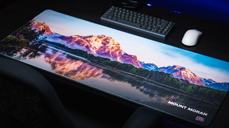 Mount Moran deskmat featuring the iconic Grand Teton peak reflected in Jackson Lake, displayed on a gaming desk with premium stitched edges and vibrant HD photography.