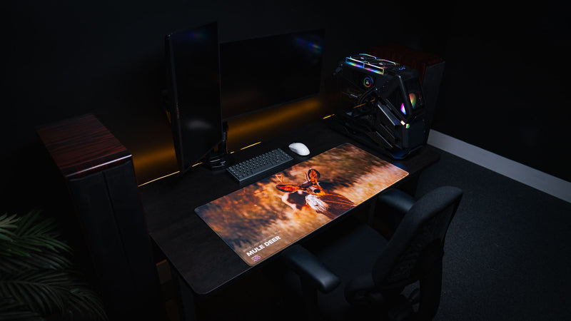 Angled overhead view of the Bryce Canyon Mule Deer Buck America 250 deskmat on a minimalist gaming desk, highlighting the oversized surface, vivid print quality, and premium stitched-edge construction.