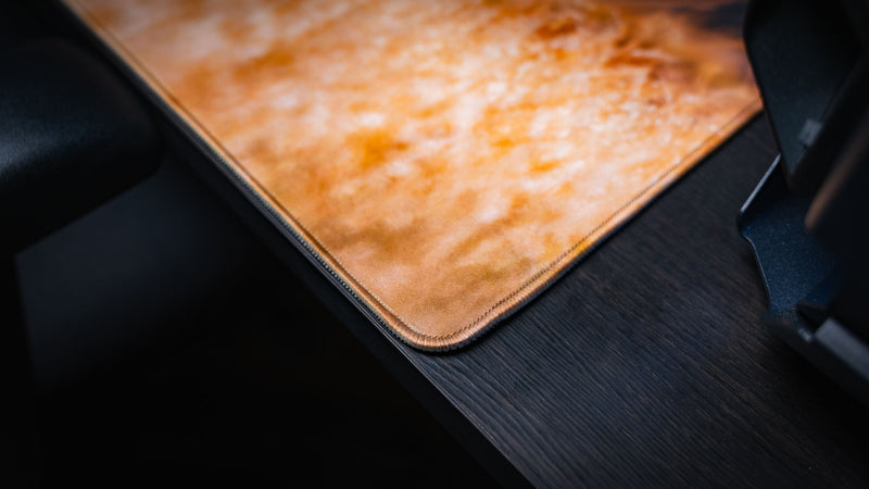 Close-up of the Mule Deer America 250 deskmat corner showing golden grass artwork, fabric texture, and premium stitched edge.