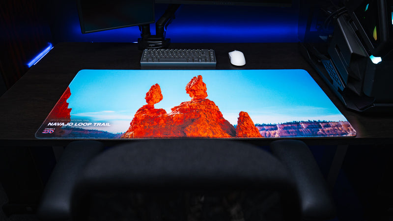 Top-down view of the Navajo Loop Trail deskmat featuring Bryce Canyon's iconic Thor's Hammer hoodoo, premium stitched edges, vibrant HD photography, and a gaming desk setup.