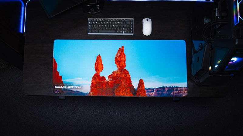 Top-down view of the Navajo Loop Trail deskmat featuring Bryce Canyon's iconic Thor's Hammer hoodoo, premium stitched edges, vivid HD photography, and a modern gaming desk setup.