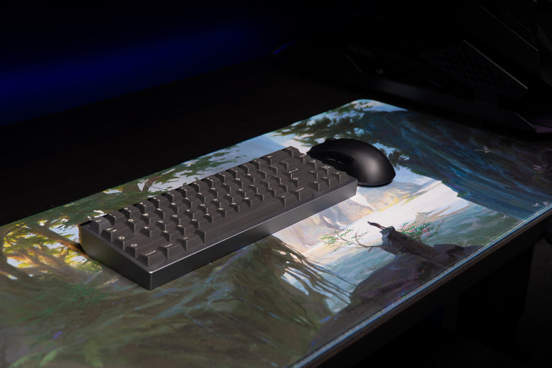Keyboard and mouse resting on the Lake of Laugg deskmat over its misty lake and lone-traveler artwork