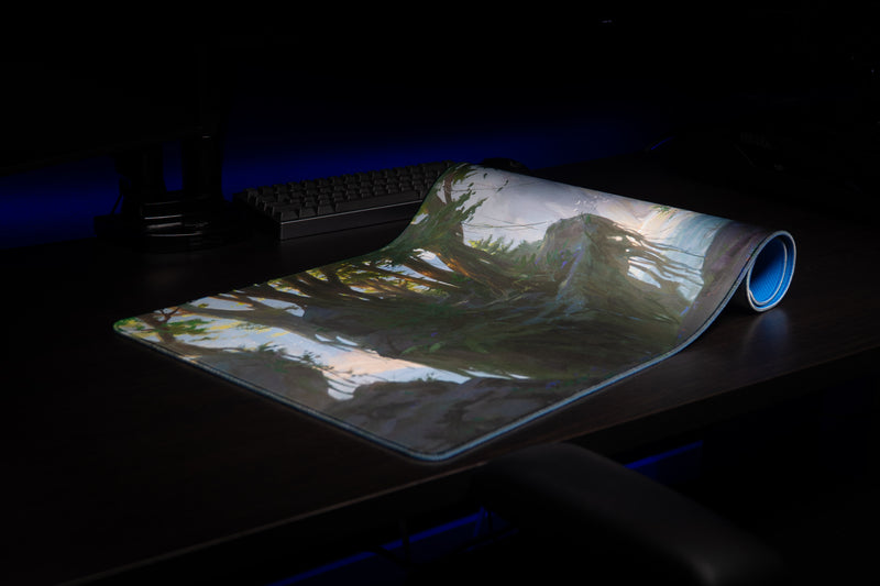 Partly rolled Lake of Laugg deskmat showing its blue underside, stitched edge, and forest artwork