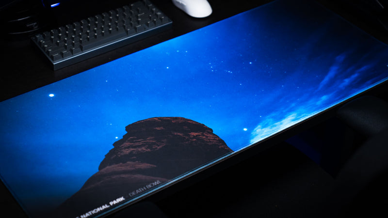 Angled view of the Nightsky Death Bowl deskmat featuring a brilliant star-filled sky above the iconic Arches National Park rock formation on a premium gaming desk setup.