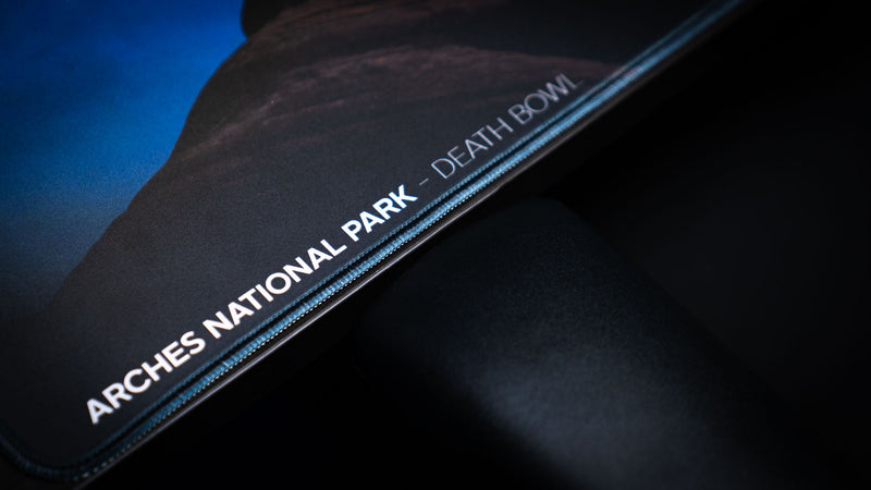 Angled view of the Nightsky Death Bowl deskmat featuring a brilliant star-filled sky above the iconic Arches National Park rock formation on a premium gaming desk setup.