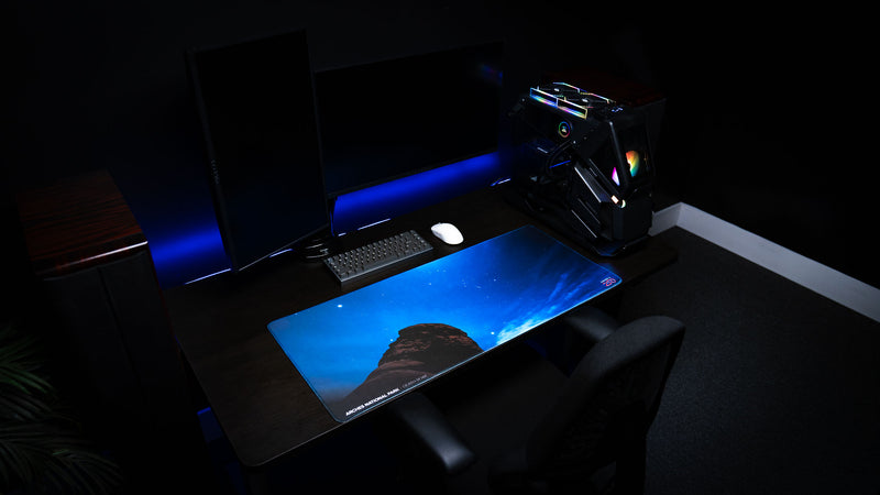 Wide-angle view of the America 250 Nightsky Death Bowl deskmat on a premium gaming desk setup, showcasing the star-filled sky over Arches National Park with a mechanical keyboard, gaming PC, and monitor.