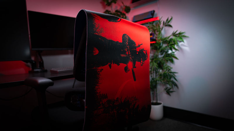 Close-up of the Nighttime Patrol Rust deskmat showcasing the flexible stitched-edge construction and vivid red artwork featuring a scientist carrying a suppressed rifle during a nighttime patrol.