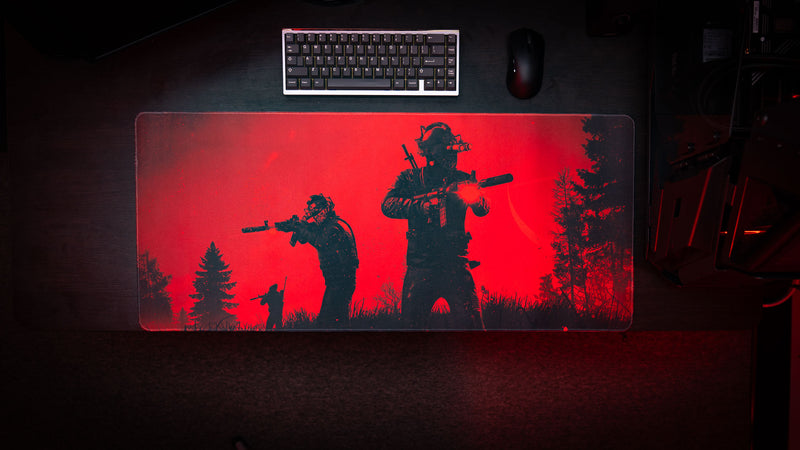 Top-down gaming desk setup featuring the Nighttime Patrol Rust deskmat with armed scientists on patrol beneath a red night sky, paired with a mechanical keyboard and gaming mouse.