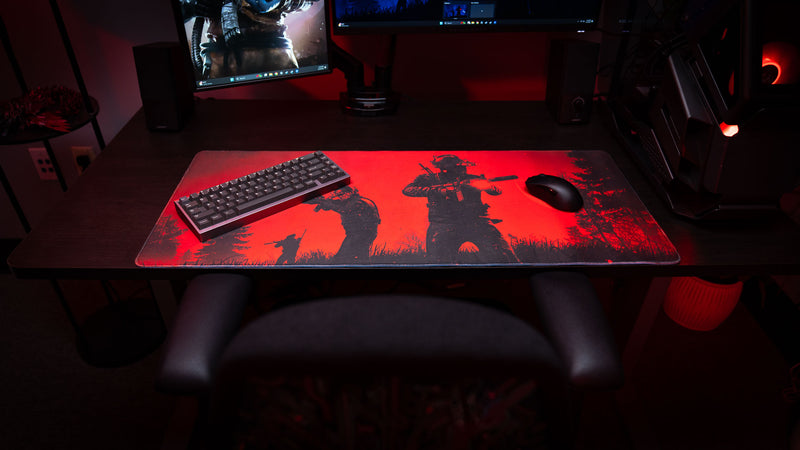 RGB gaming setup featuring the Nighttime Patrol Rust deskmat with silhouetted scientists patrolling through a forest under a crimson night sky, displayed with a mechanical keyboard, gaming mouse, and PC tower.