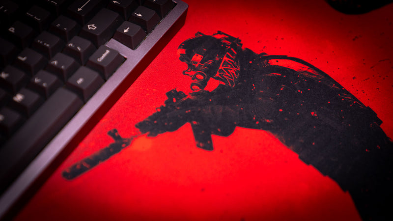 Close-up detail of the Nighttime Patrol Rust deskmat featuring a heavily armed scientist aiming a suppressed rifle under a vivid red night sky, showcasing the textured print and tactical artwork.
