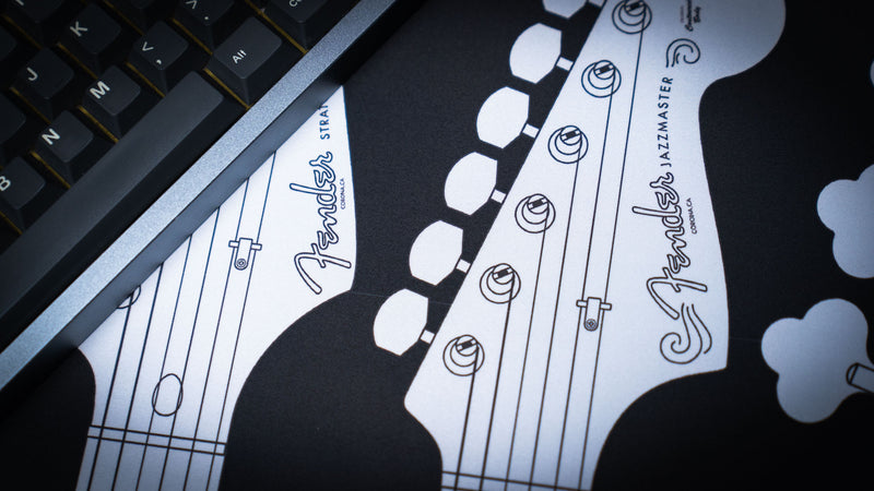 Close desk view of the Fender logo and illustrated headstocks on the black XXL desk mat