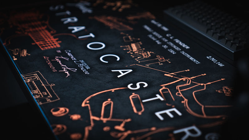Angled view of the gold Fender Stratocaster Blueprint XXL desk mat and warm copper linework
