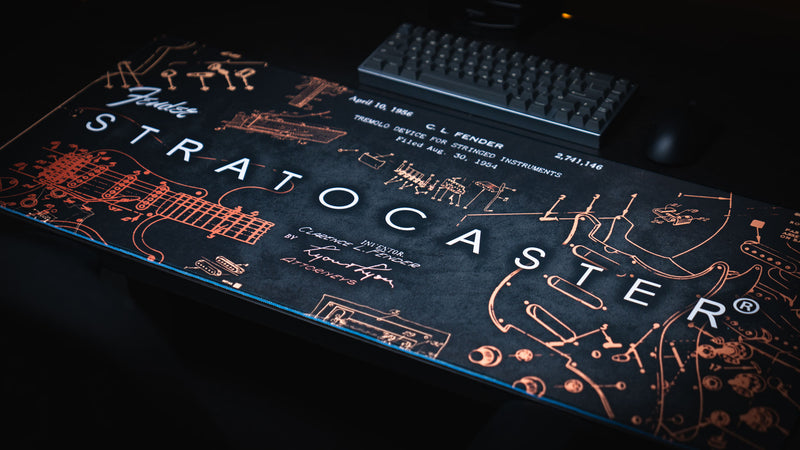 Gold Fender Stratocaster Blueprint XXL desk mat shown beneath a keyboard and mouse in a desktop setup