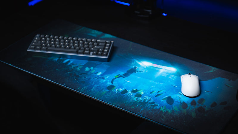 Official Rust Labs Breach deskmat shown from an angled view, featuring an underwater diver exploring Rust's Labs monument with vibrant blue lighting, sea life, and premium stitched edges.