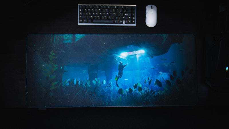 Top-down view of the Official Rust Labs Breach deskmat featuring an underwater diver beneath the Labs monument with vibrant ocean artwork, mechanical keyboard, and gaming mouse.