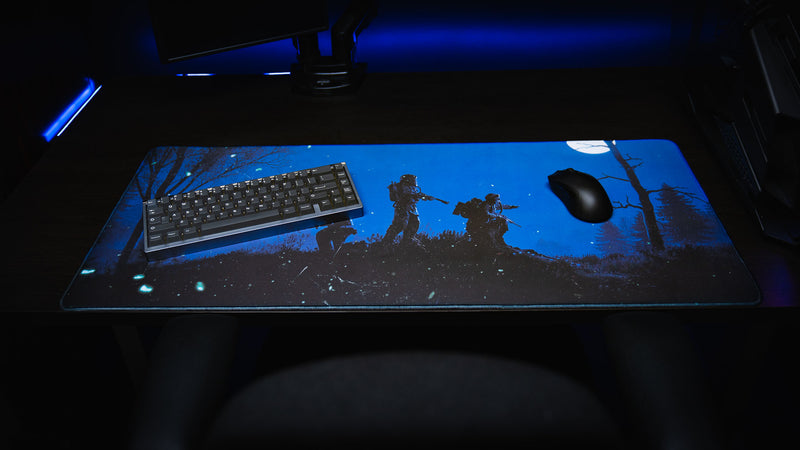 Official Rust Twilight Roam deskmat displayed in a gaming setup with a compact mechanical keyboard and gaming mouse on a moonlit nighttime scene.