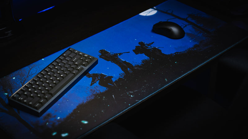 Official Rust twilight Roam deskmat displayed with a compact mechanical keyboard and gaming mouse, featuring hazmat survivors beneath a moonlit forest sky.